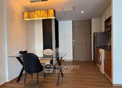 Modern dining area with glass table, stylish chairs, and compact kitchen featuring appliances.