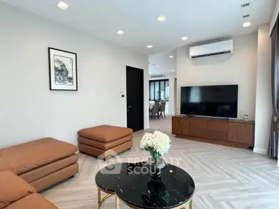 Modern living room with stylish furniture and large TV, open layout to dining area.