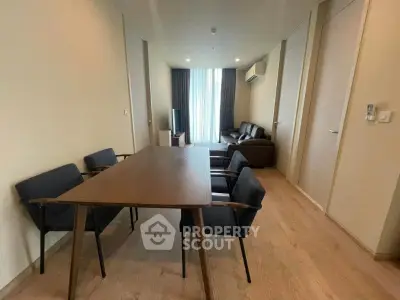 Modern living room with dining area, wooden flooring, and natural light from large window.