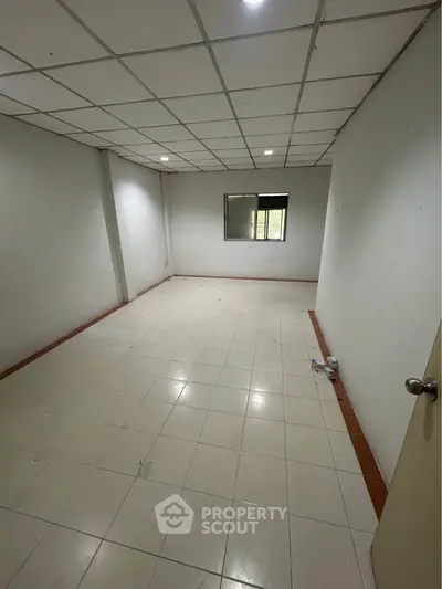 Spacious empty room with tiled flooring and window, ideal for customization.