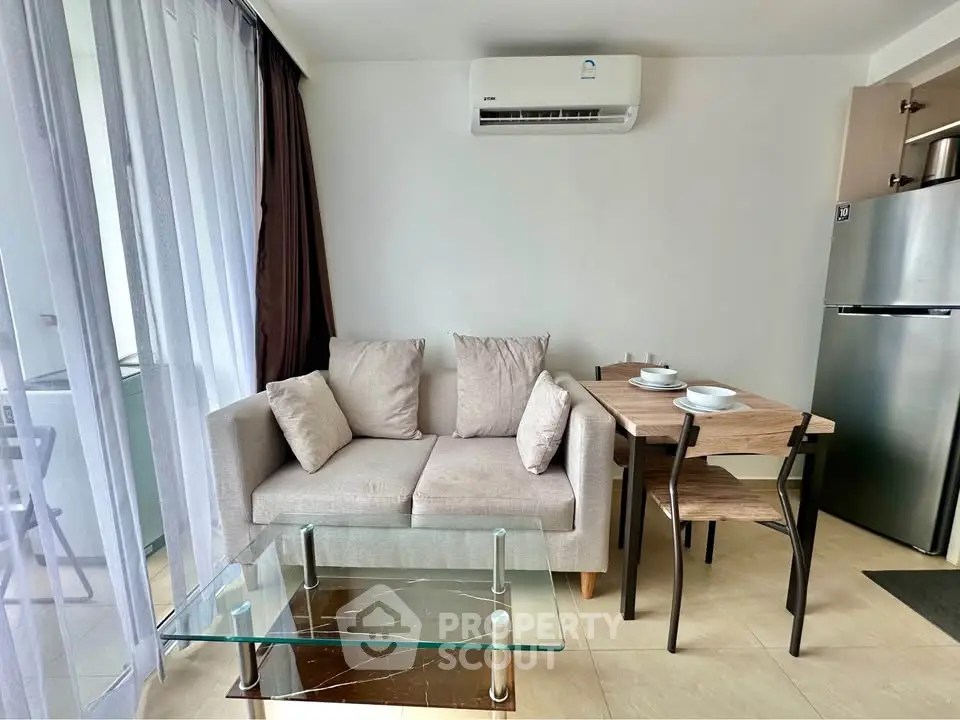 Modern living room with cozy sofa, glass coffee table, and dining area in open layout apartment.