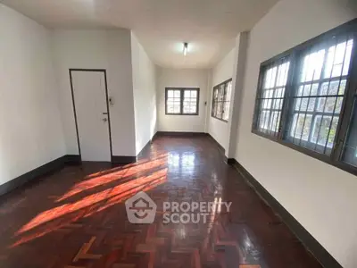 Spacious empty room with polished wooden floors and large windows offering natural light.