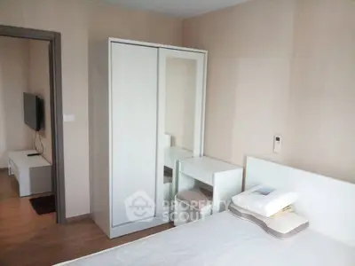 Modern bedroom with sleek white furniture and wall-mounted TV in a cozy apartment.