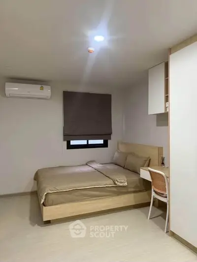 Modern minimalist bedroom with wooden bed and study desk, featuring air conditioning and neutral decor.