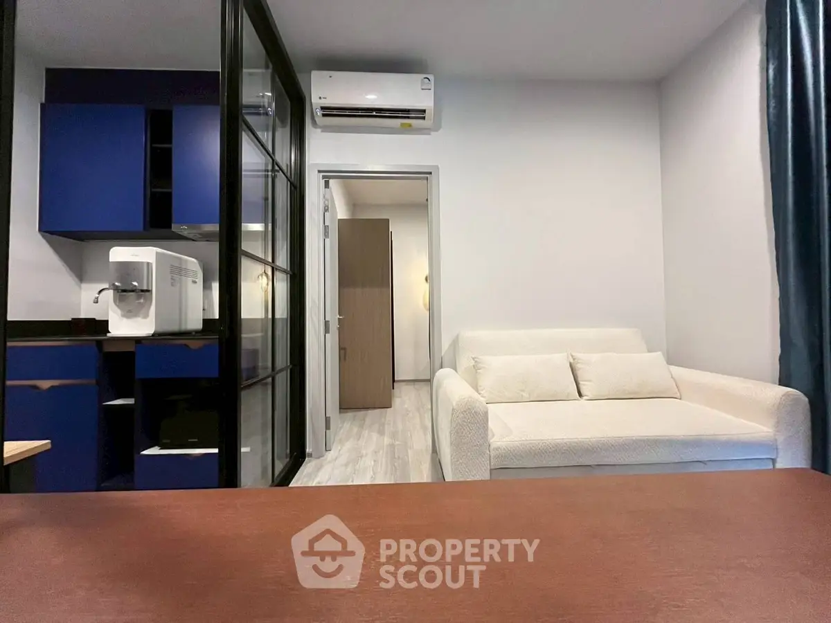 Modern living room with sleek design and compact kitchen area, featuring a cozy white sofa and stylish blue cabinets.