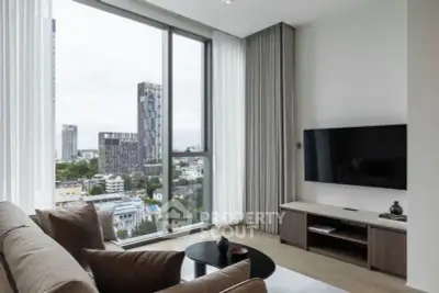 Modern living room with large windows and city view, featuring a sleek TV setup and cozy seating.