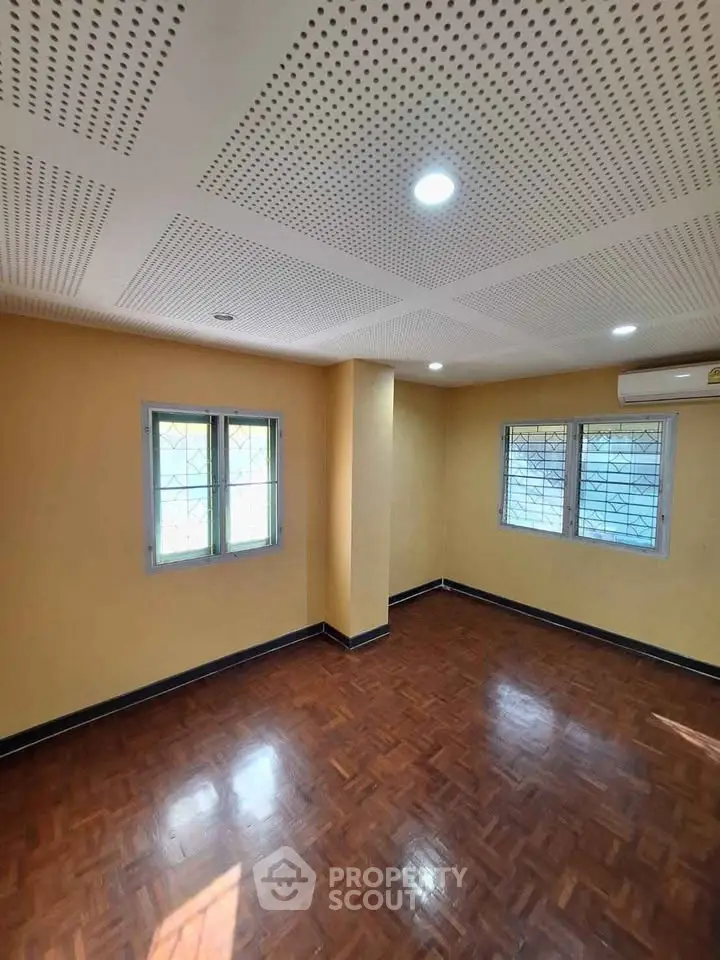 Spacious empty room with wooden flooring and bright windows, perfect for customization.