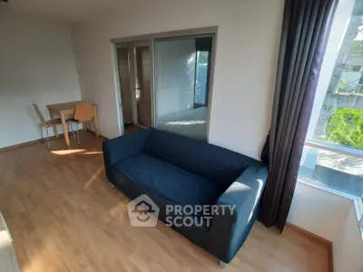 Spacious living room with modern sofa and dining area, featuring large windows for natural light.