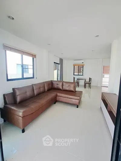 Spacious modern living room with sleek brown leather sectional and dining area, perfect for entertaining.