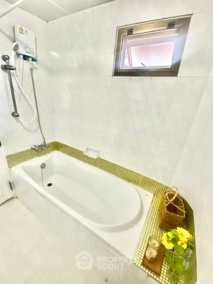 Bright bathroom with bathtub and window, featuring white tiles and decorative elements.
