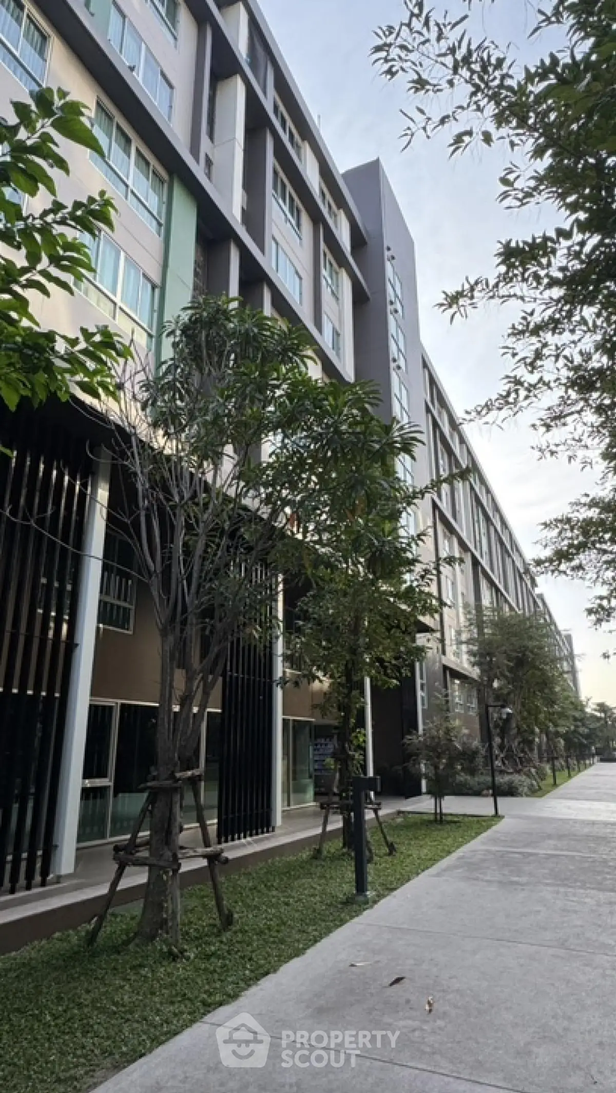 Modern apartment building exterior with lush greenery and sidewalk