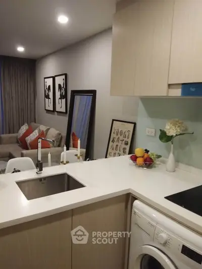 Modern kitchen with sleek design, integrated washing machine, and cozy living area in open layout apartment.
