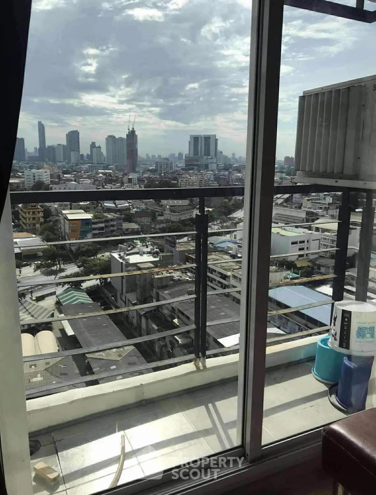 Stunning cityscape view from high-rise balcony with glass railing and air conditioning unit.