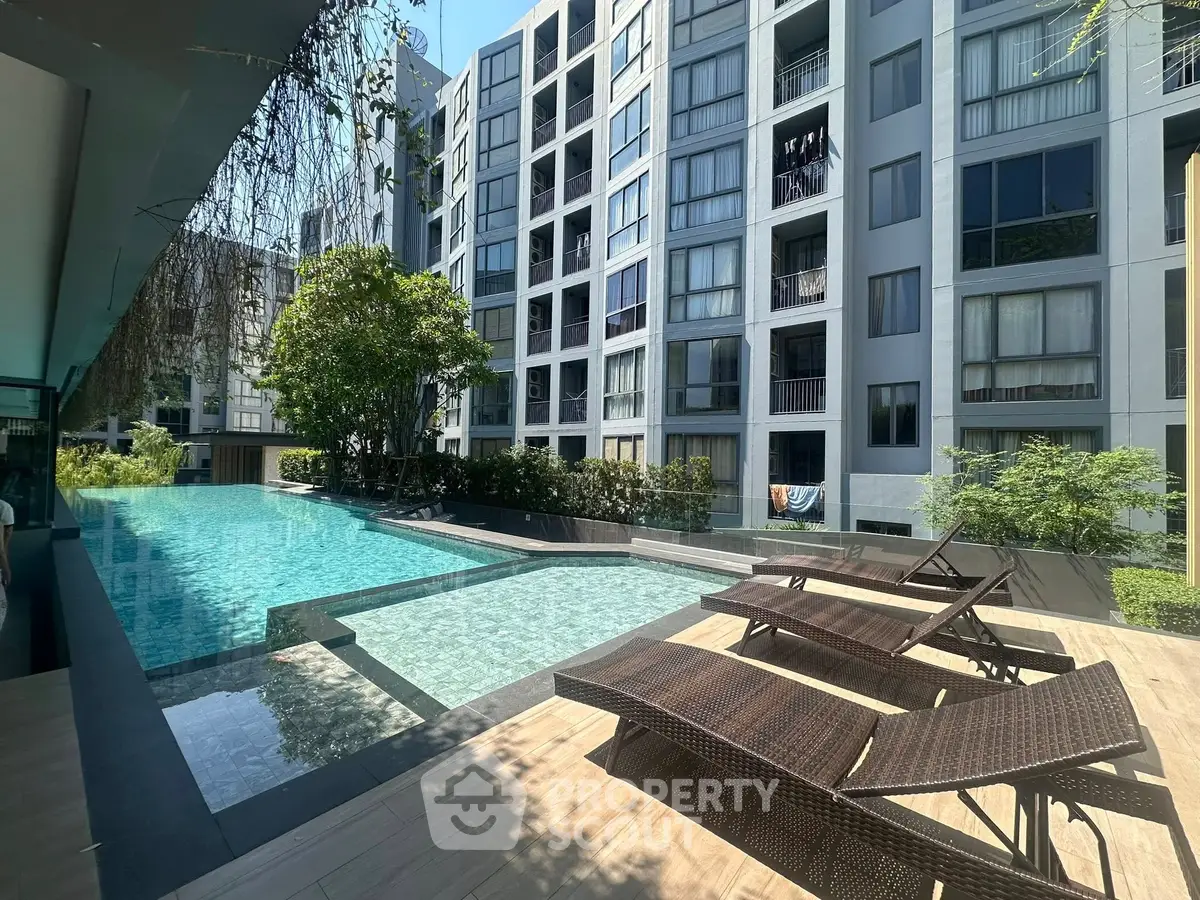 Modern apartment complex with a luxurious pool and sun loungers, perfect for relaxation and leisure.