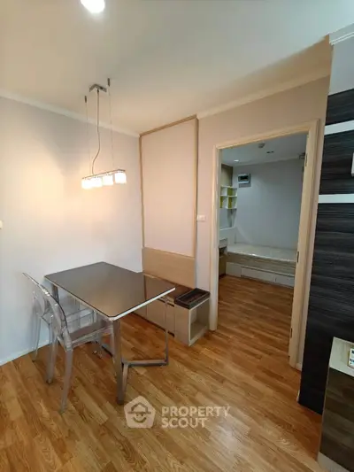 Modern dining area with sleek table and chairs, leading to cozy bedroom with wooden flooring.