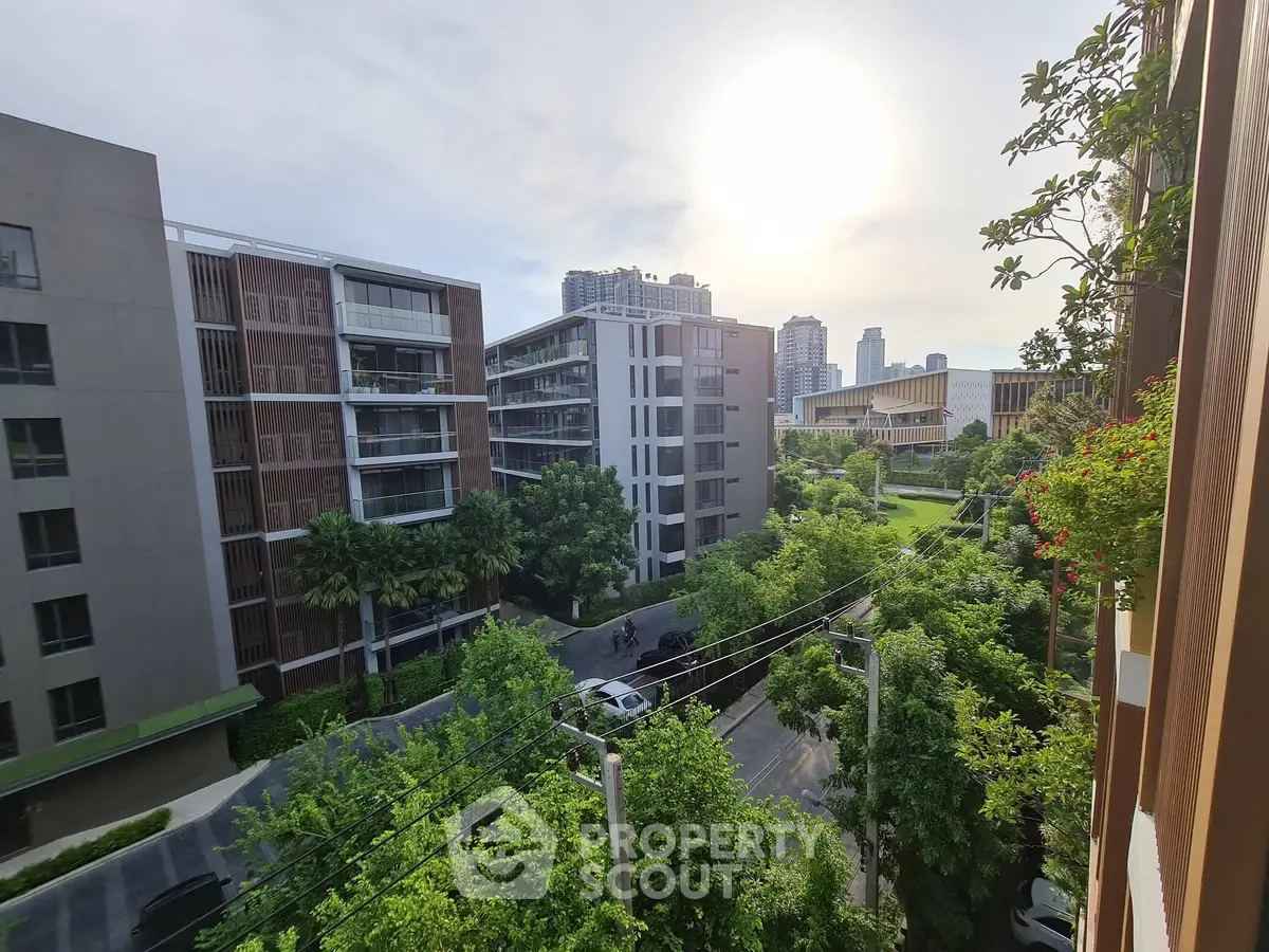 Stunning urban view from a modern apartment balcony overlooking lush greenery and contemporary buildings.
