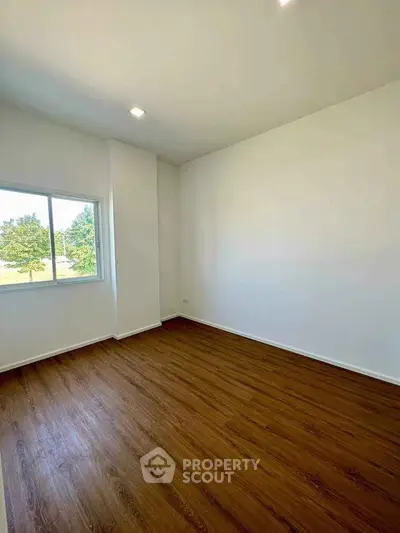 Spacious empty room with wooden flooring and large window offering natural light and scenic view.