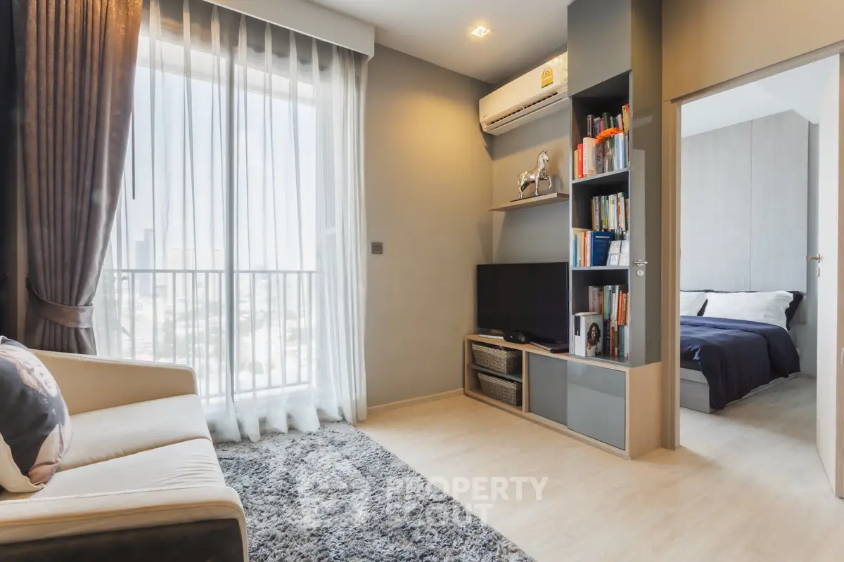 Modern living room with cozy decor and natural light, featuring a TV and bookshelf.