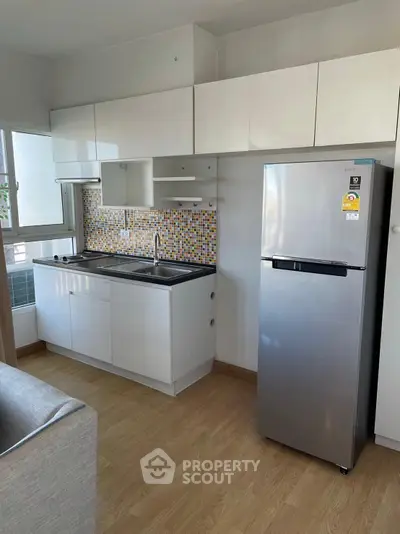 Modern kitchen with sleek cabinets and stainless steel fridge in a cozy apartment.