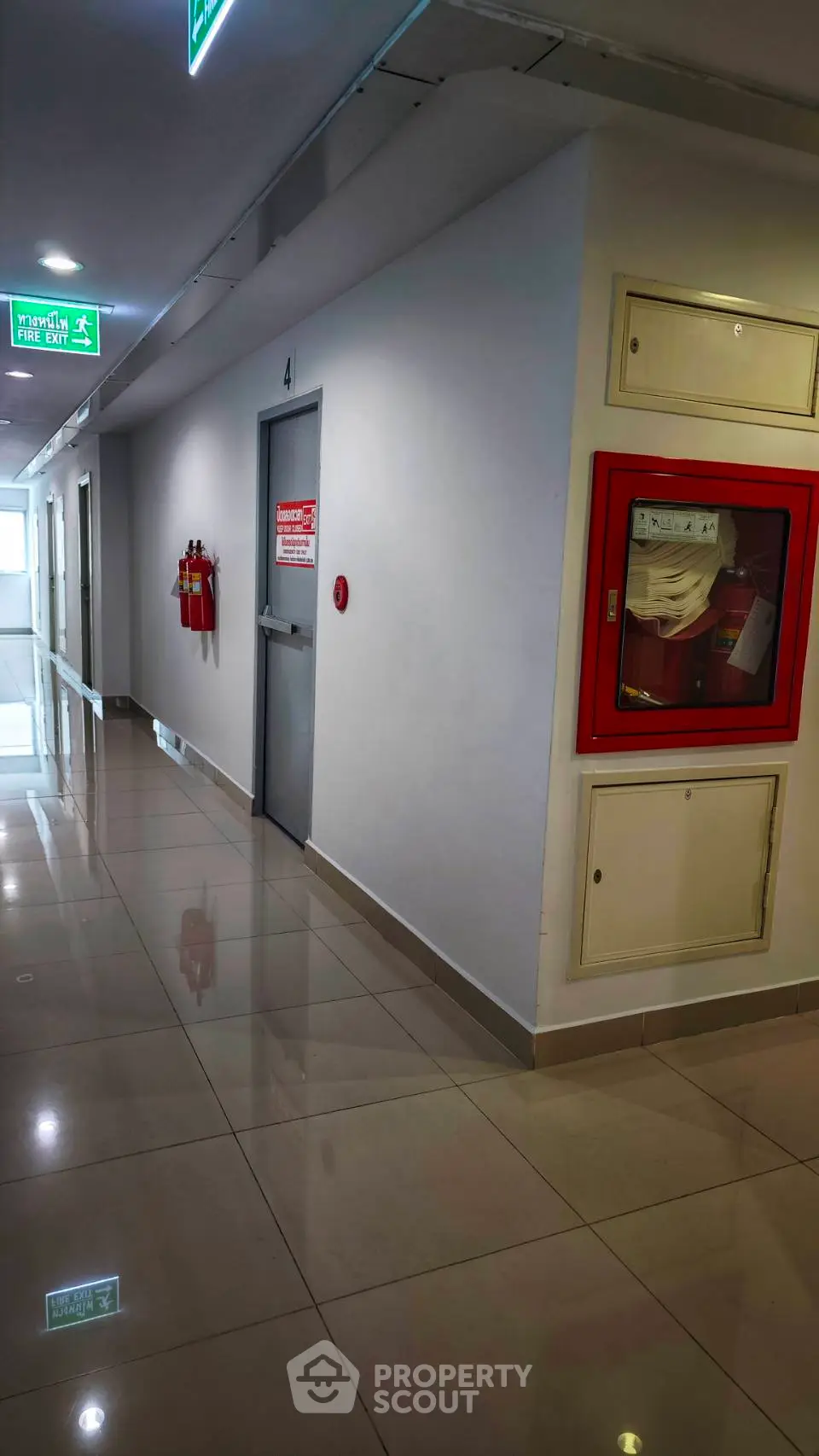 Modern building corridor with fire safety equipment and emergency exit signs.