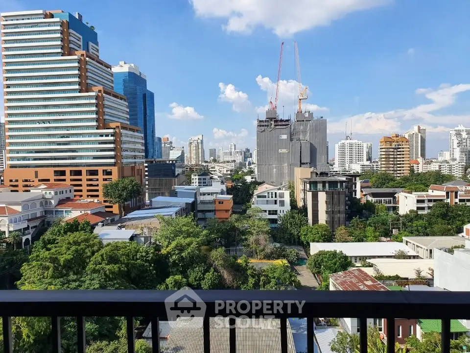 Stunning cityscape view from balcony with lush greenery and modern buildings under blue sky.