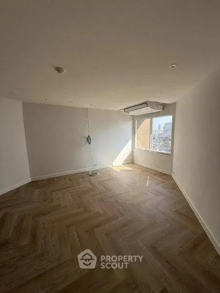 Spacious empty room with wooden flooring and large window offering natural light.