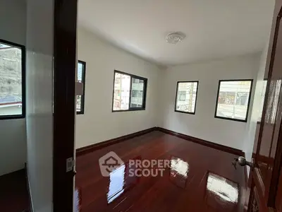 Spacious room with polished wooden floors and multiple windows for natural light.