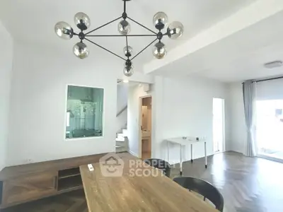 Modern dining area with stylish chandelier and wooden table in a bright open-plan space.