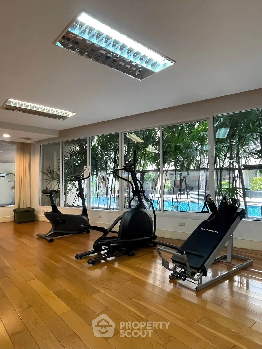 Spacious gym with modern equipment and pool view in luxury apartment complex.