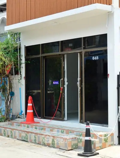 Modern building entrance with glass doors and tiled steps, featuring safety cones and chain barrier.