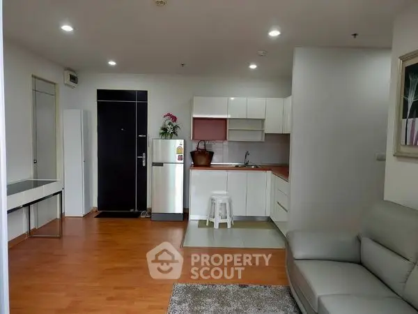 Modern open-layout living room with kitchen, featuring sleek furniture and wooden flooring.