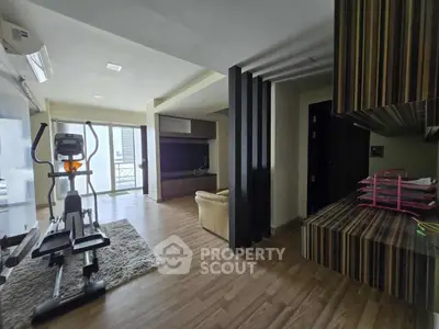 Spacious living room with exercise equipment and modern decor, featuring a large window for natural light.