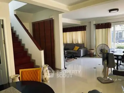 Spacious living room with modern decor and natural light, featuring a cozy seating area and elegant staircase.