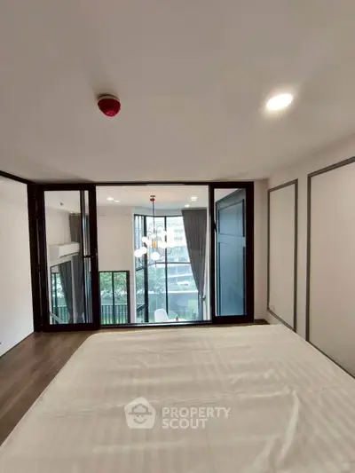 Spacious bedroom with large windows and balcony view in modern apartment.