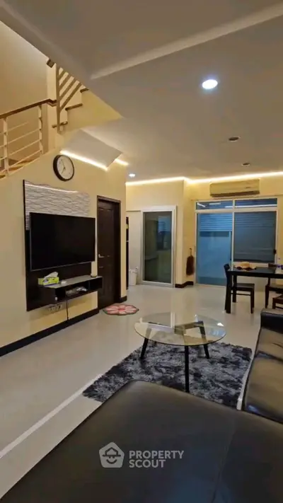 Modern living room with sleek furniture and open layout, featuring a wall-mounted TV and stylish decor.