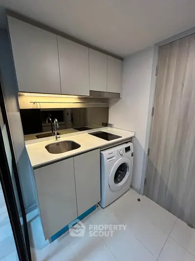 Compact kitchen with washing machine and sleek cabinetry in modern apartment.