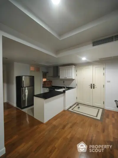 Modern kitchen with stainless steel appliances, polished hardwood floors, and ample white cabinetry, seamlessly opening into a cozy living space.