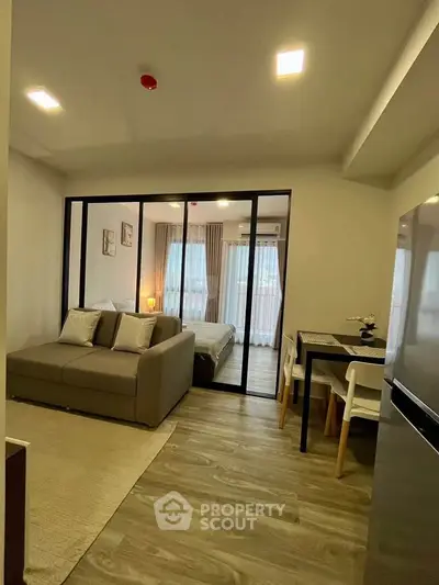 Modern open-plan living room with cozy sofa and dining area leading to a stylish bedroom.