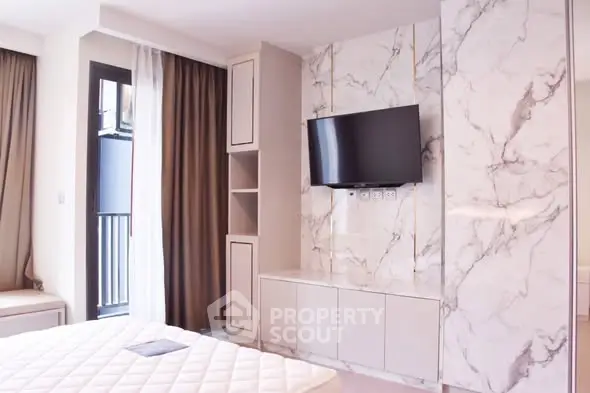 Modern bedroom with marble accent wall and mounted TV, featuring elegant design and natural light.
