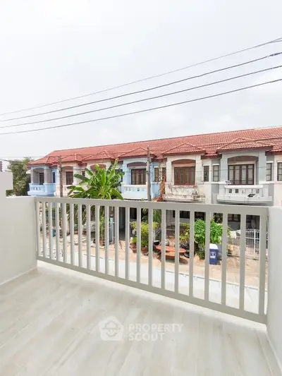 Charming balcony view overlooking row of townhouses with red roofs and lush greenery.