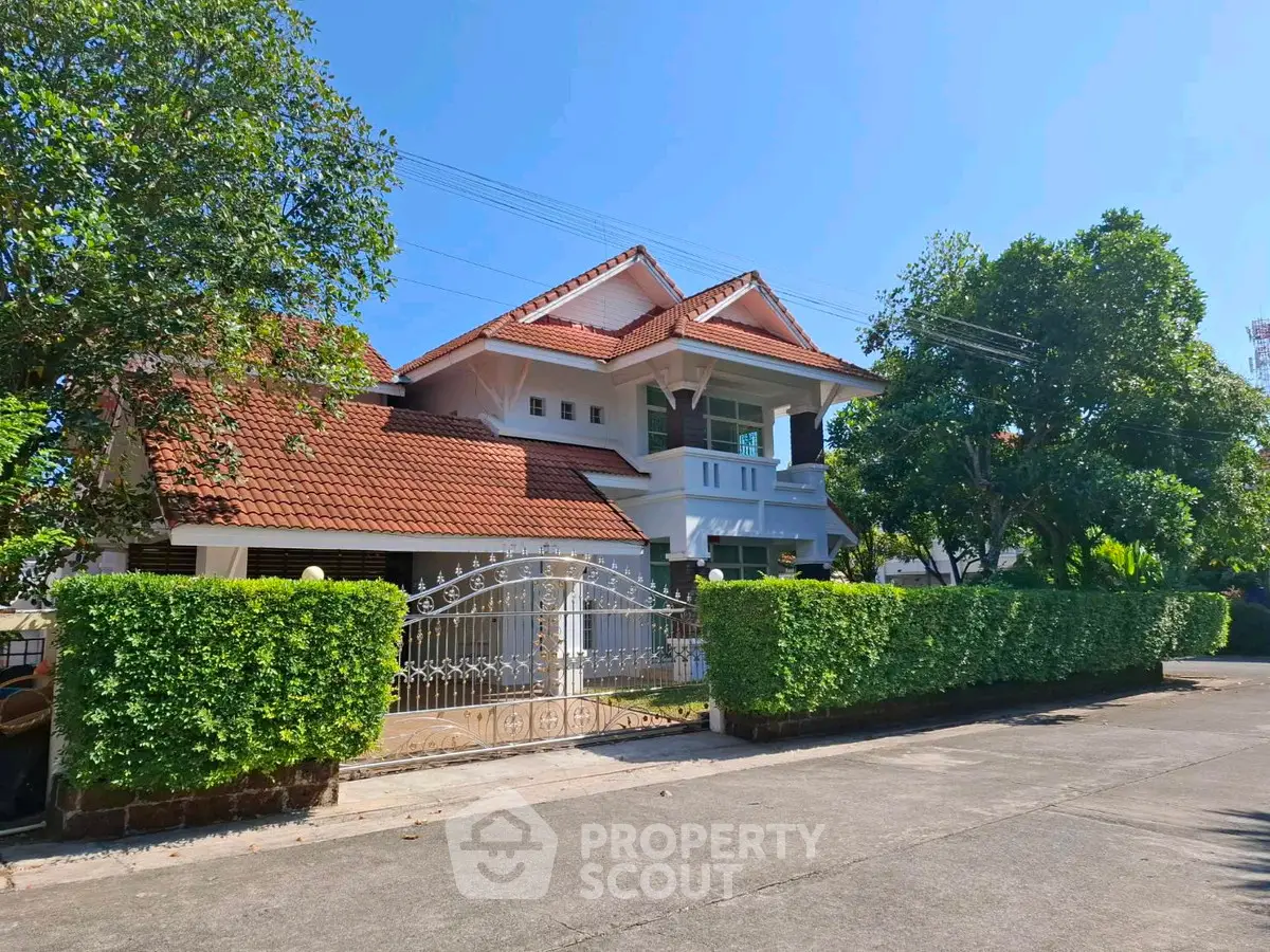 Charming two-story house with red-tiled roof and lush greenery in a serene neighborhood.