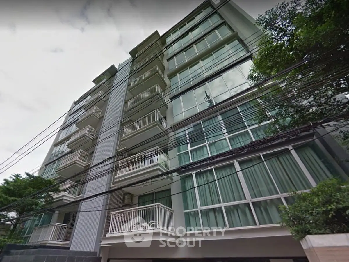 Modern multi-story building with large windows and balconies in urban setting.