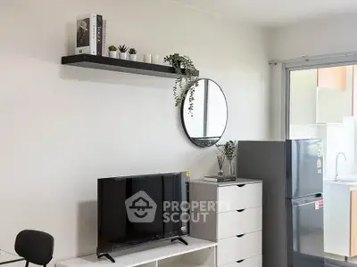 Modern living room with sleek TV setup and stylish decor, featuring a compact kitchen area with fridge.