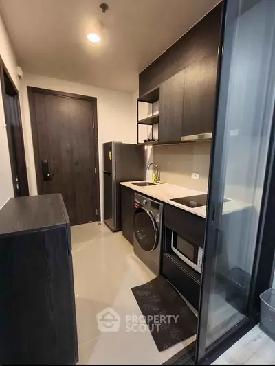 Modern compact kitchen with sleek appliances and dark cabinetry in a stylish apartment.