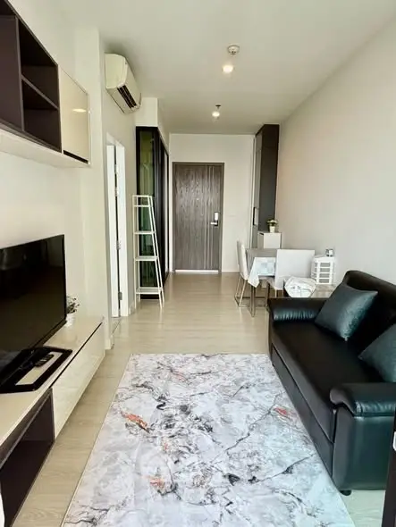 Modern living room with sleek black sofa, stylish TV unit, and elegant dining area in open-plan apartment.