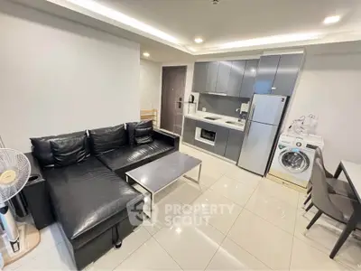 Modern open-plan living room with sleek kitchen and appliances, featuring a cozy black leather sofa.