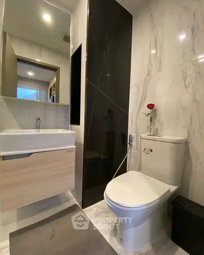 Modern bathroom with sleek design, featuring a stylish sink and toilet, accented by a single red rose.