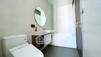 Modern bathroom with sleek fixtures and a minimalist design, featuring a round mirror and a stylish vanity.