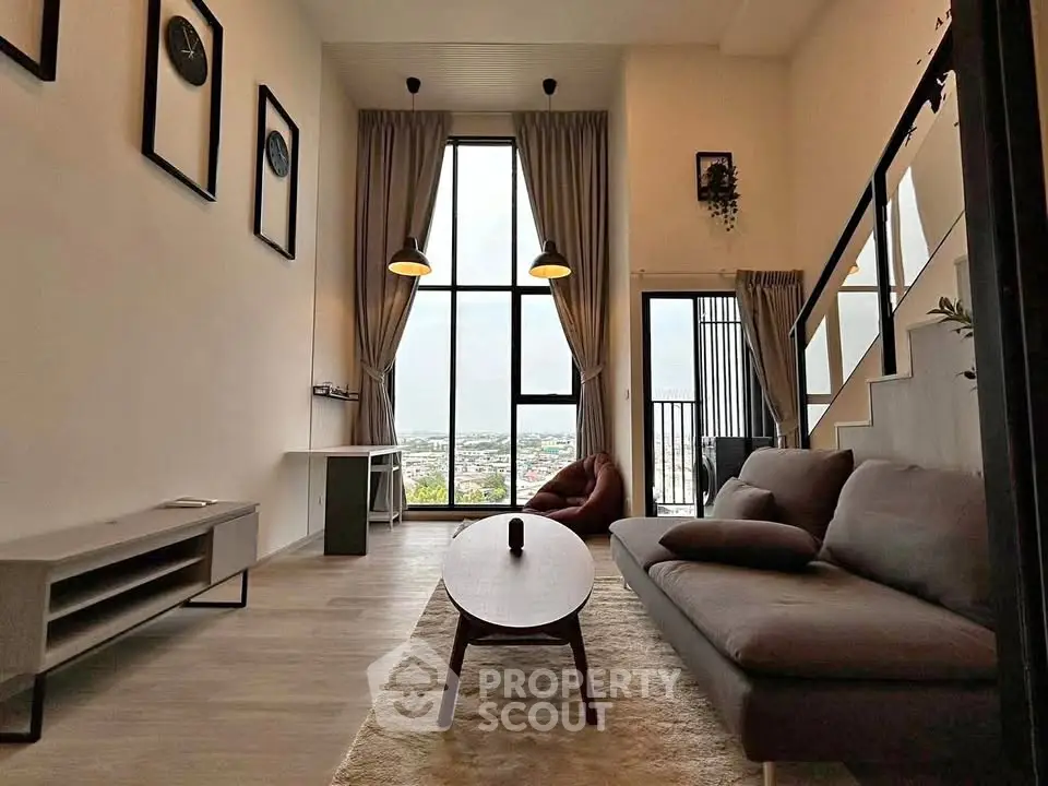 Modern living room with high ceiling and large windows offering stunning city views.
