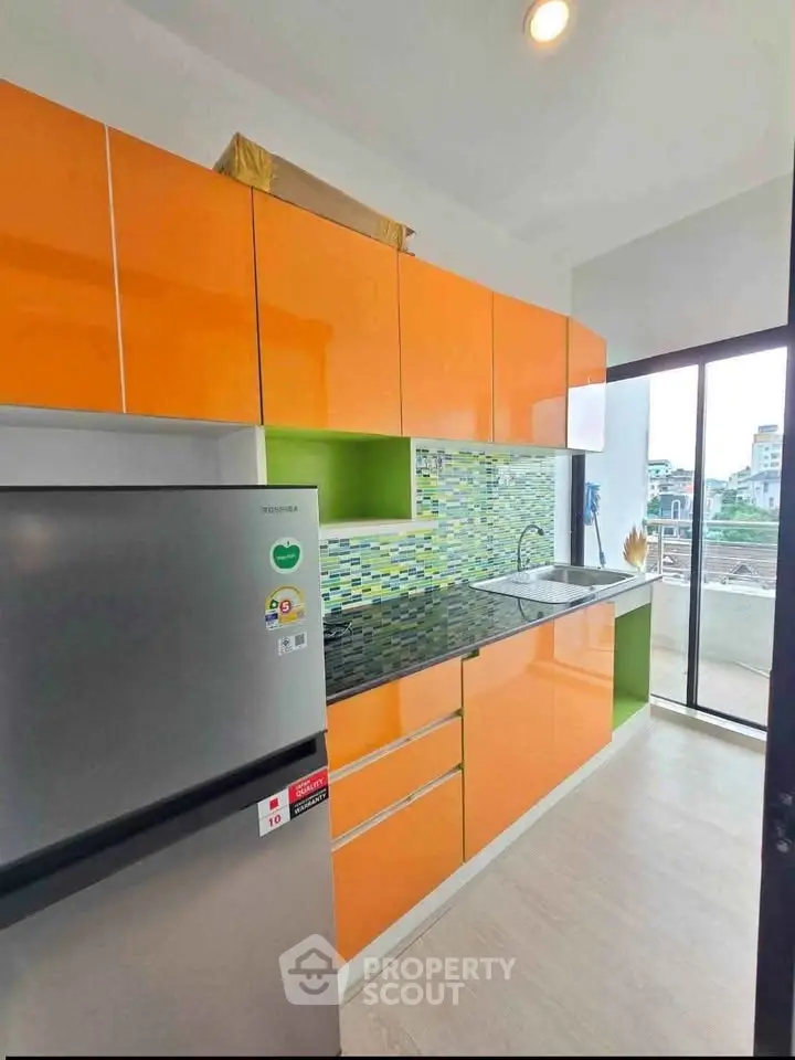 Modern kitchen with vibrant orange cabinets and city view from window.